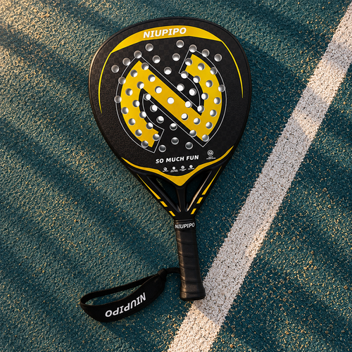 Niupipo black and gold 18K diamond padel racket on a teal court, with its black wrist strap. AI-styled product image.